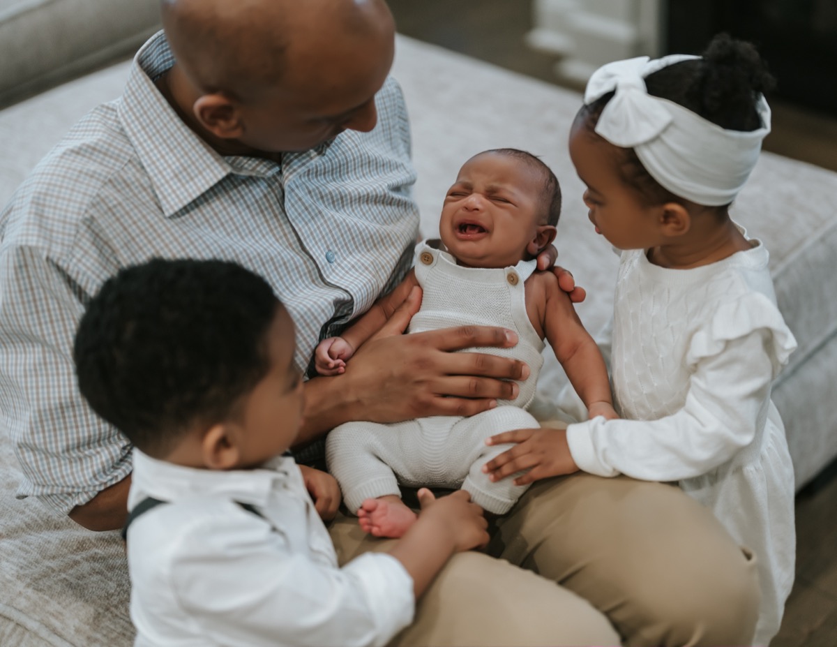 Father holding crying newborn Yohannes while Yonas and Yohanna lean in close to comfort him