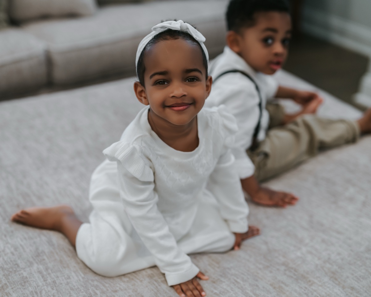 Yohanna in white dress and headband smiling at the camera, with Yonas sitting behind her on the couch