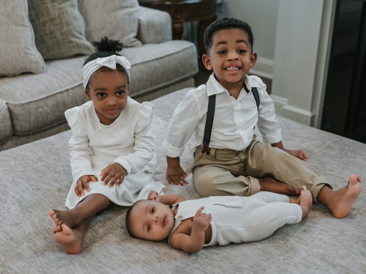 Yohanna and Yonas smiling at the camera while baby Yohannes lies in front of them looking at the lens