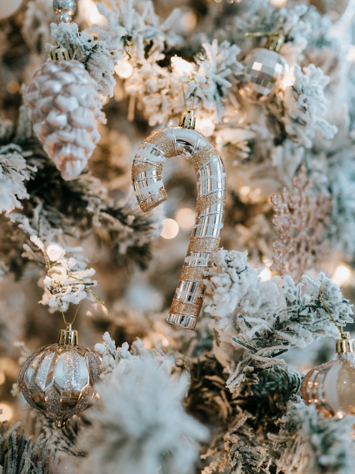 Close-up of a glass candy cane ornament with gold glitter stripes on the frosted Christmas tree