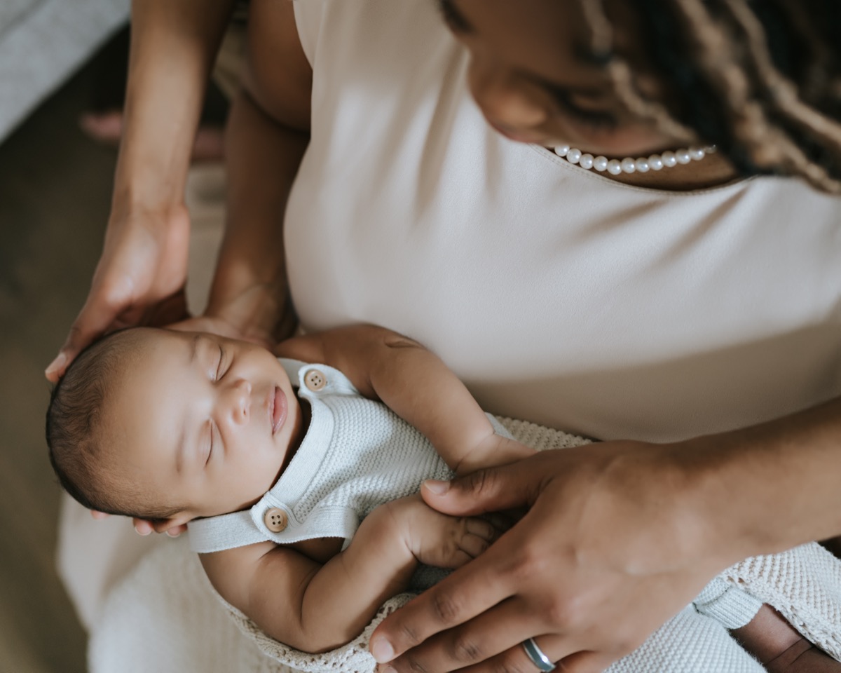 Tender close-up of mother's hands cradling sleeping newborn Yohannes on a knit blanket