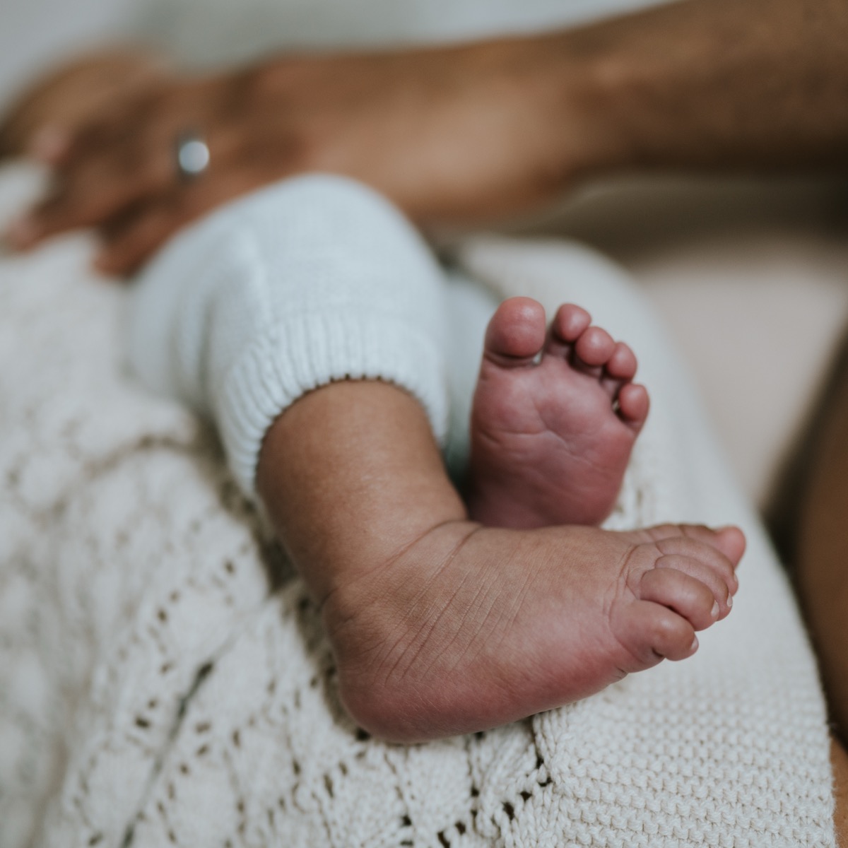 Close-up of newborn Yohannes's tiny feet in knit pants, resting on a cream blanket