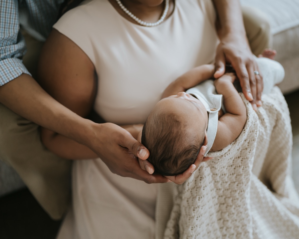 Parents' hands together gently cradling sleeping newborn Yohannes's head on a knit blanket