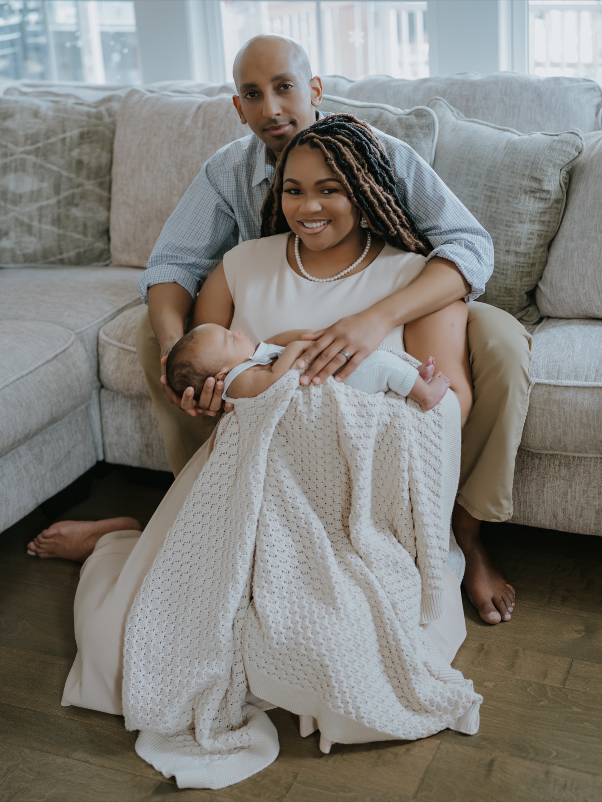 Both parents smiling at the camera, mother holding newborn Yohannes in a blanket on the floor by the couch