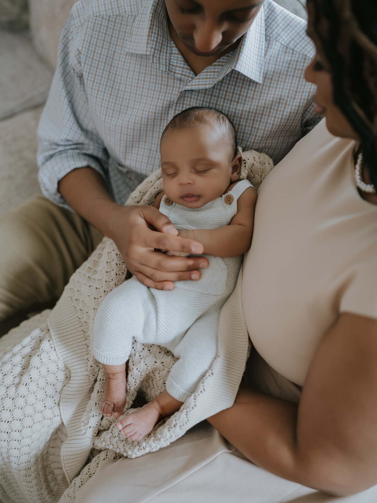 Both parents looking down at sleeping newborn Yohannes cradled in father's arms on a knit blanket