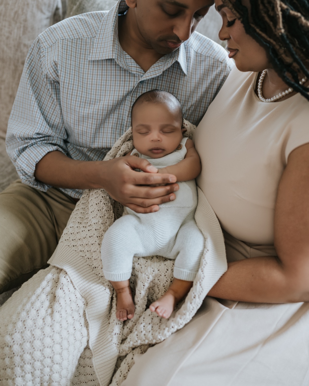 Parents gazing down at sleeping newborn Yohannes cradled in father's hands with a knit blanket